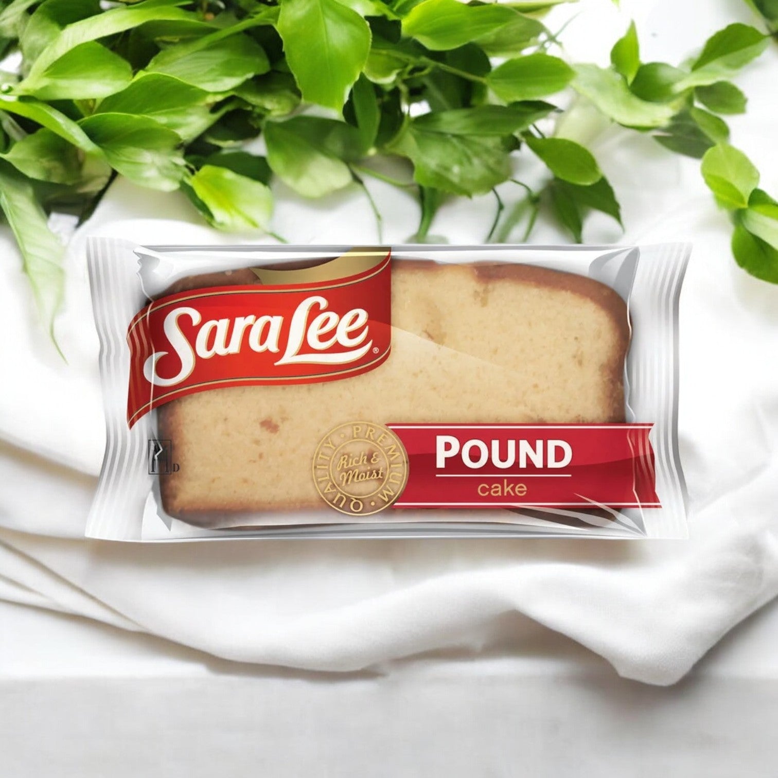 A packaged slice of Easy Lunches Sara Lee Pound Cake, 1.75 oz., placed on a white cloth with green leaves in the background, showcases its rich buttery flavor and moist texture. Available in a case containing 24 counts!