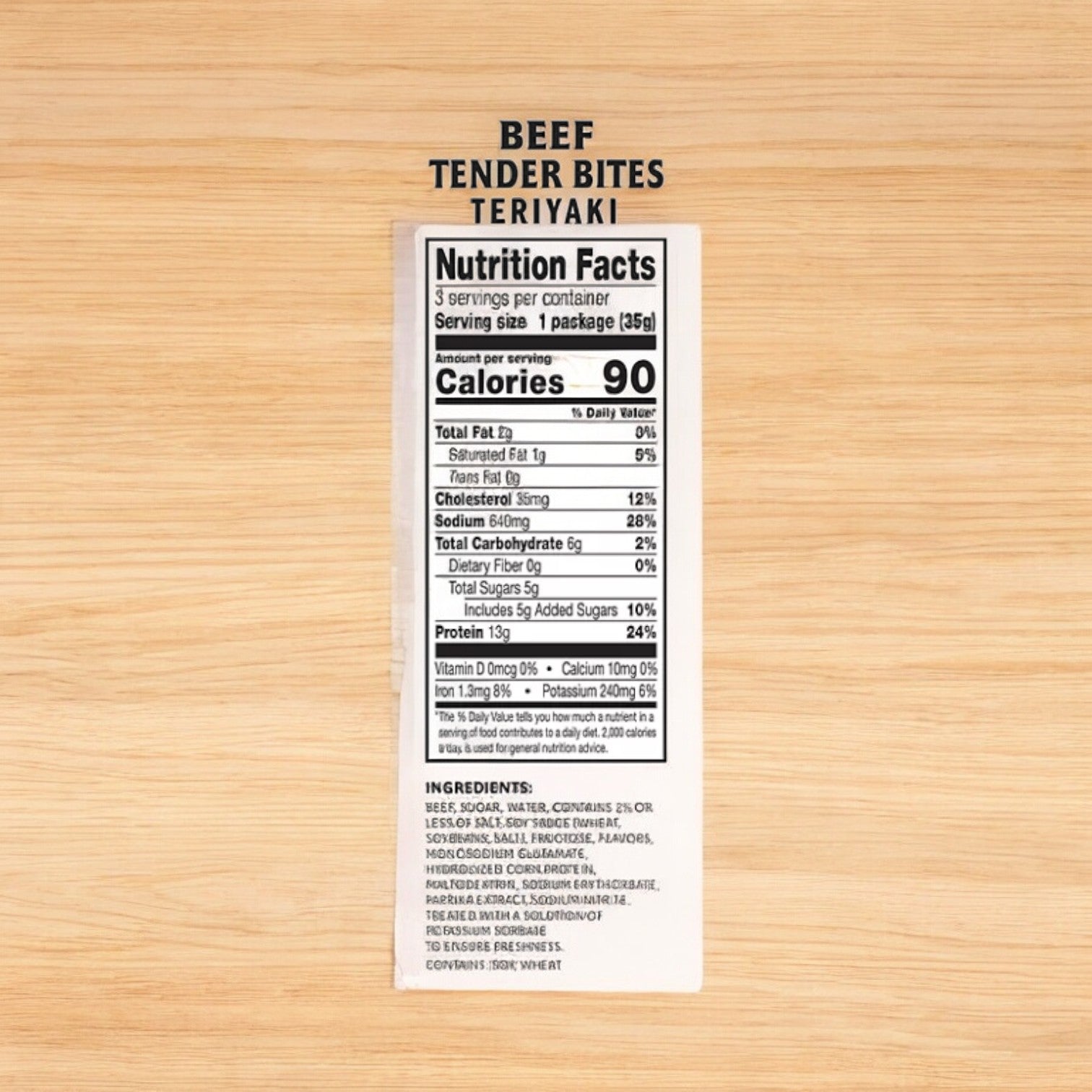 Image of a nutrition facts label for Jack Link's Beef Tender Bites Teriyaki - 1.25 oz on a wooden surface. The label highlights 90 calories per serving and lists detailed nutritional information and ingredients, perfect for adding to your Jack Link's meat snacks Variety Pack.