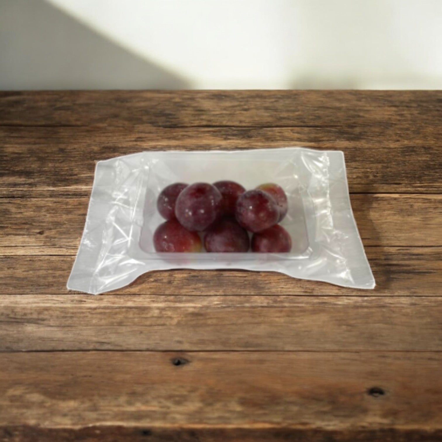 A sealed plastic package containing Easy Lunches' Red Seedless Grapes, 2.5 oz., rests on a rustic wooden surface, ensuring freshness for 7 days.