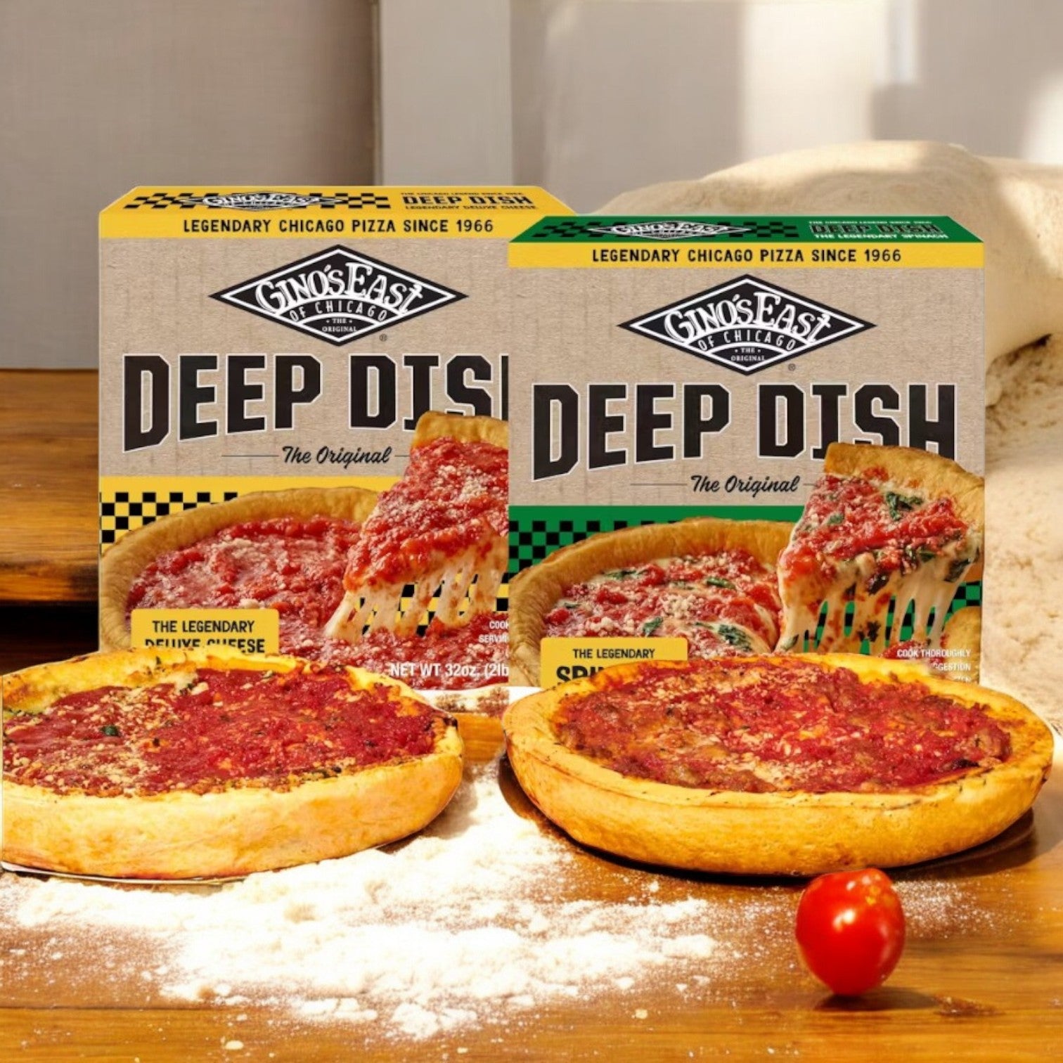 Two boxes of Gino's East Deluxe Cheese & Spinach Deep Dish Pizza Combo are displayed alongside a baked cheese pizza and a topped slice on a wooden surface, embodying true Chicago-style flavor. A single tomato and scattered flour add to the scene.