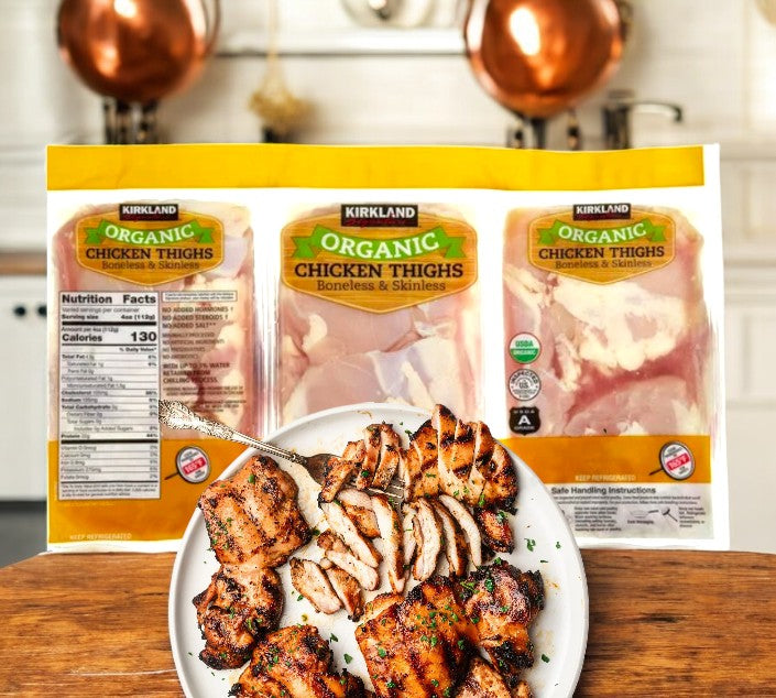 The Kirkland Signature Organic Boneless Skinless Chicken Thighs-1 Count sits behind a plate of succulent, seasoned chicken pieces on a kitchen counter, offering a delicious source of lean protein for your meals.