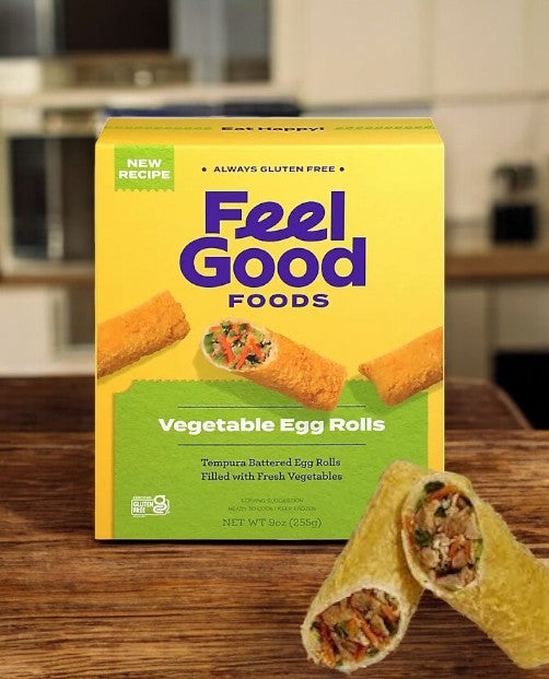 A box of Feel Good Foods Gluten-Free Vegetable Egg Rolls, 9 oz, with two egg rolls in front. The packaging emphasizes fresh vegetables, allergen-friendly qualities, and a new recipe.