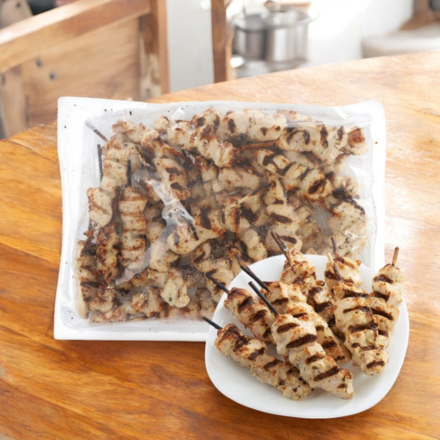 Sysco Chicken Breast Skewers, grilled and halal, on a small white plate with more skewers sealed in a Sysco bag on a wooden table.