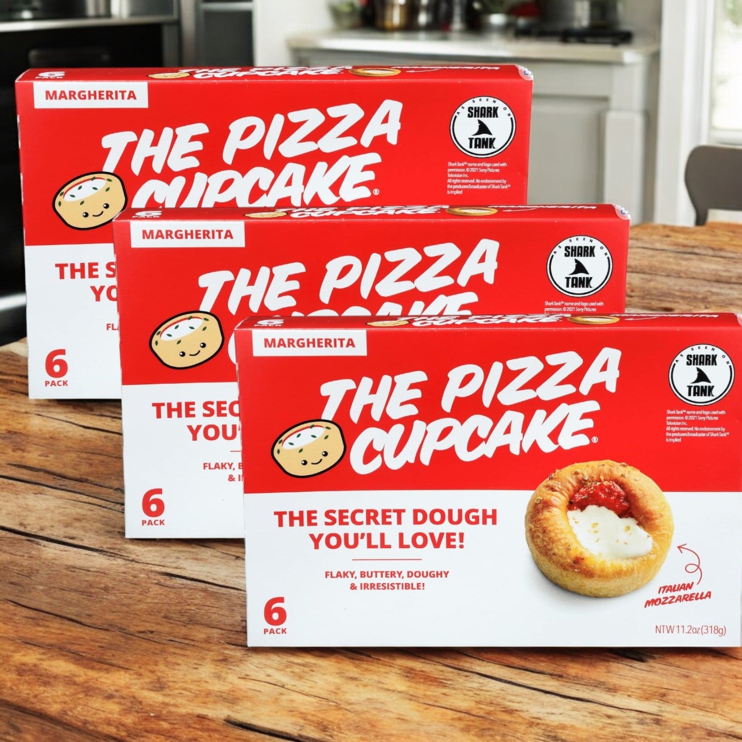 Three boxes of The Pizza Cupcake Margherita- 3 Count by The Pizza Cupcake are displayed on a kitchen table, each holding three mozzarella-filled pastries—an ideal party appetizer.