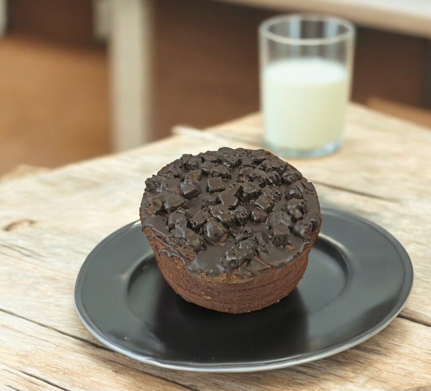 A slice of Sweet Street Uncut Chocolate Layer Cake sits on a black plate, highlighting the rich flavor of premium chocolate desserts, with a glass of milk in the background on a wooden surface.