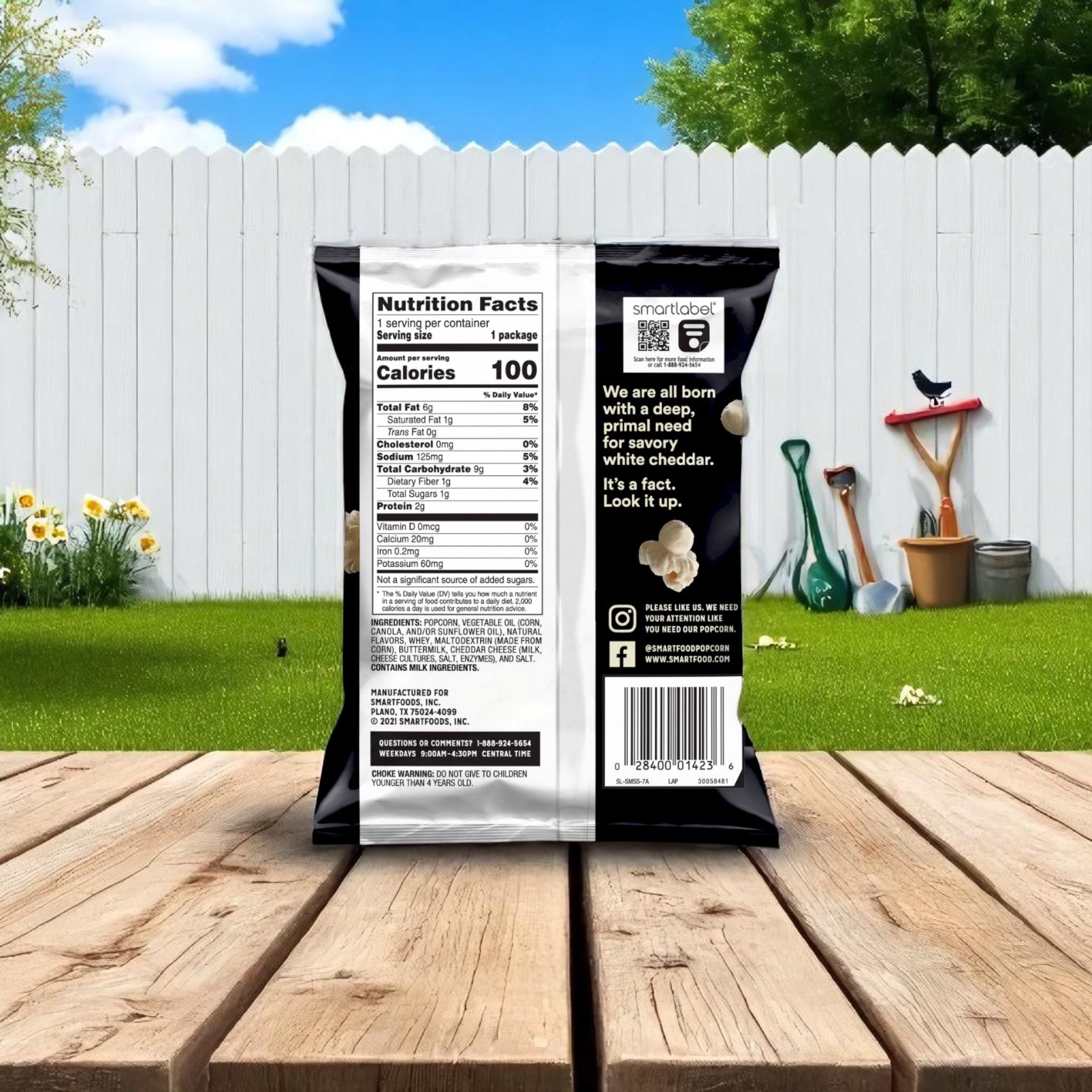 A 1 oz. Easy Lunches Smart Food Popcorn Cheddar White, from a 64-case pack, sits on a backyard table near garden tools and a white fence—nutrition facts and cheddar flavor make it the perfect on-the-go snack.