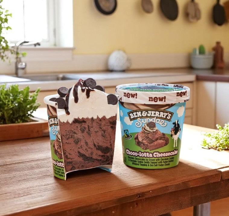 A carton of Ben & Jerry’s Ice Cream, Choco-Lotta Cheesecake Sundae (14.4 FL Oz) by Ben & Jerry's sits beside a cross-section displaying chocolate ice cream, cheesecake, whipped topping, and chocolate curls.
