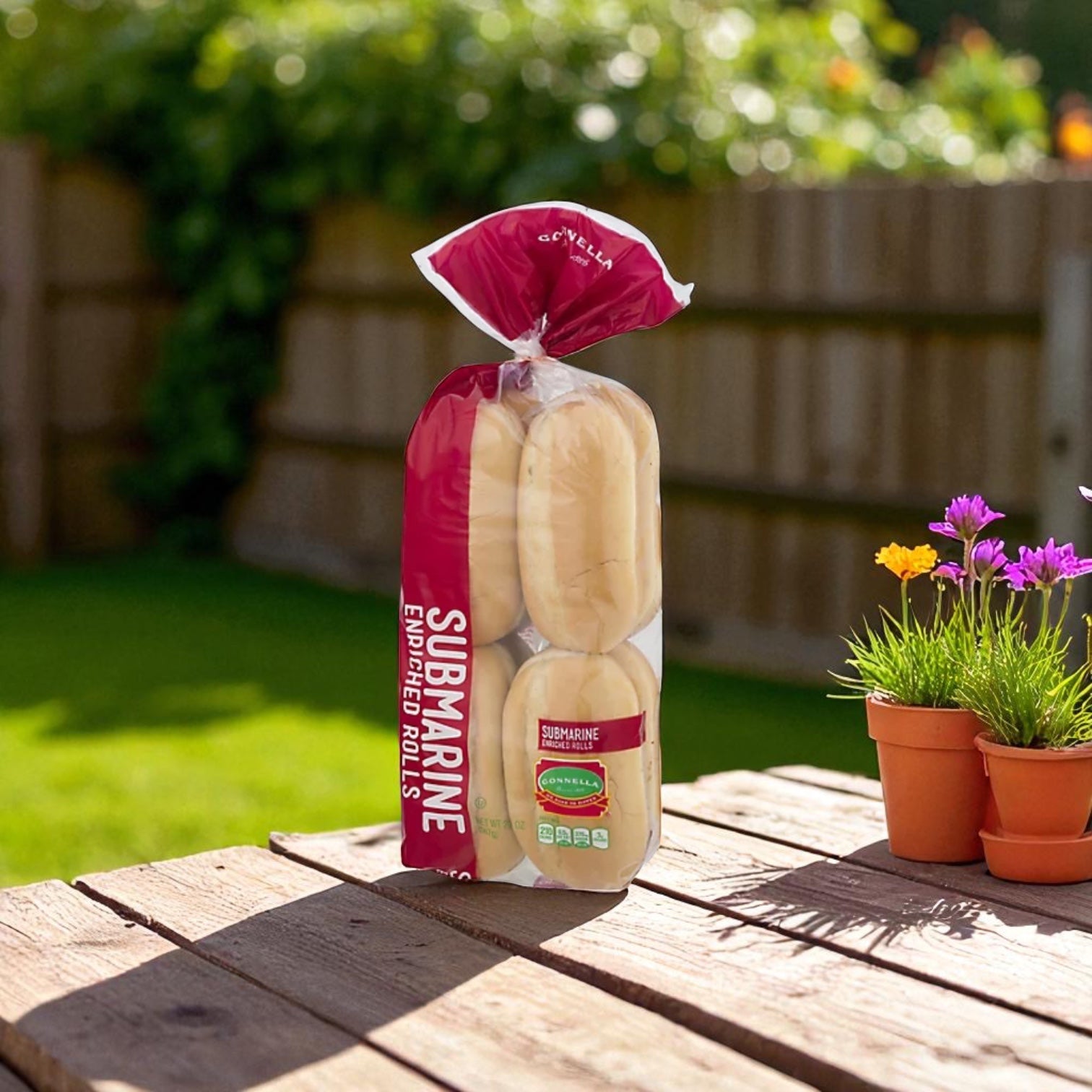 A Papa Charlie's Gonella Bread Mild Giardiniera Italian Beef Sandwich Kit (3 Count) sits on a wooden table outdoors by two small flowering plants, ideal for Chicago-style sandwiches, with grass and a fence in the background.