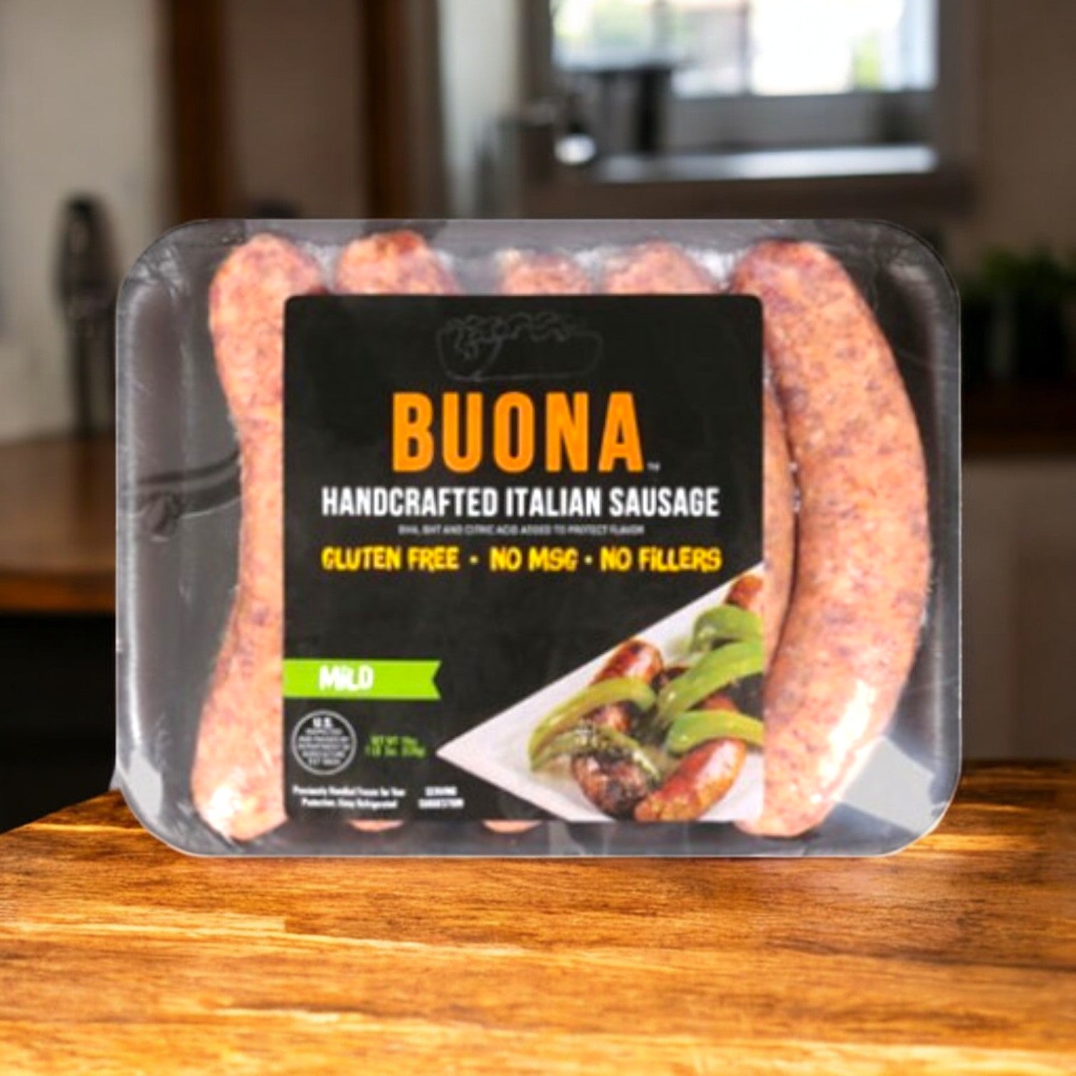 A 19 oz package of Buona Italian Sausage – Handcrafted, Mild sits on a wooden surface in a cozy kitchen, labeled gluten free with no MSG or fillers.