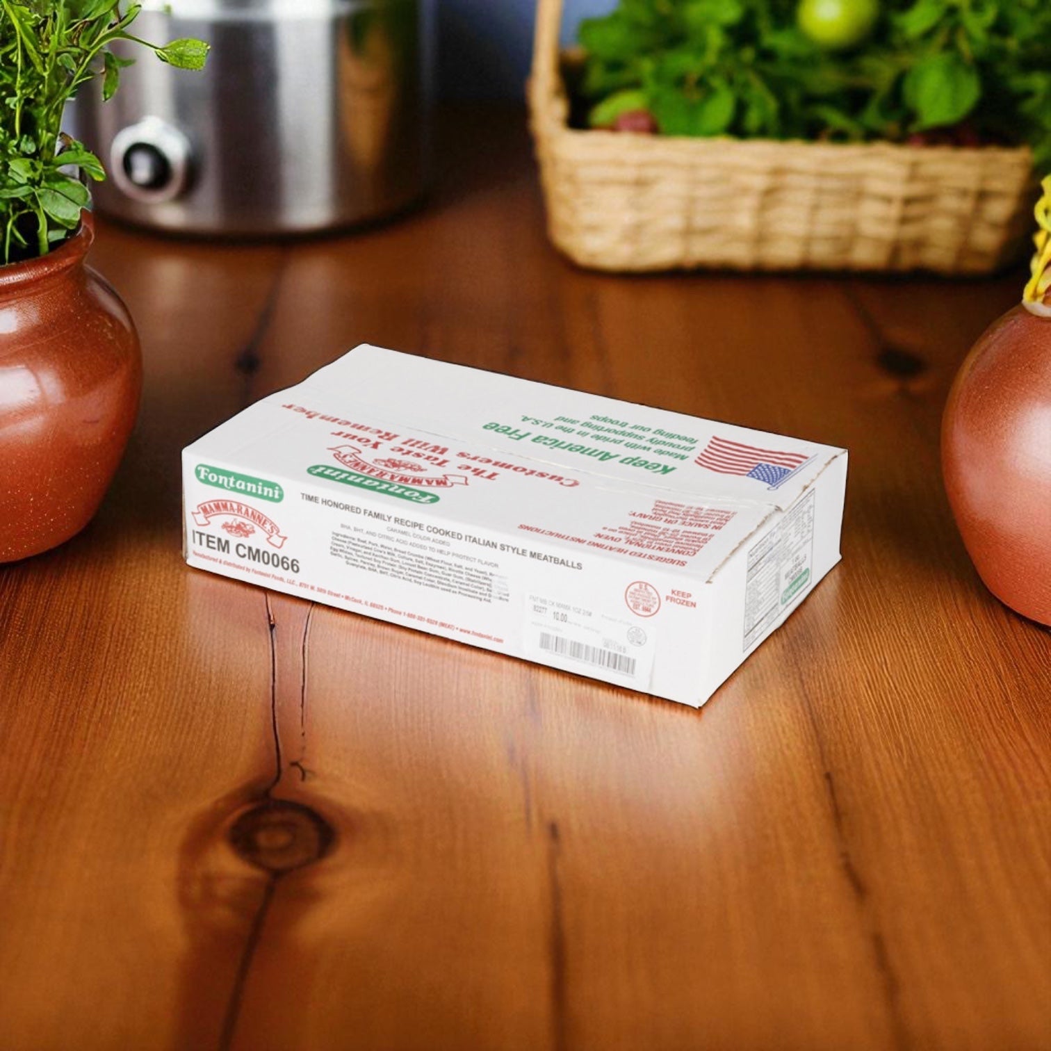 A rectangular box of Sysco Fontanini Italian Beef Pork Fully Cooked Meatballs (1 oz, 5 lb, 2 count) sits on a wooden table among potted plants, highlighting these flavorful meatballs ideal for foodservice.