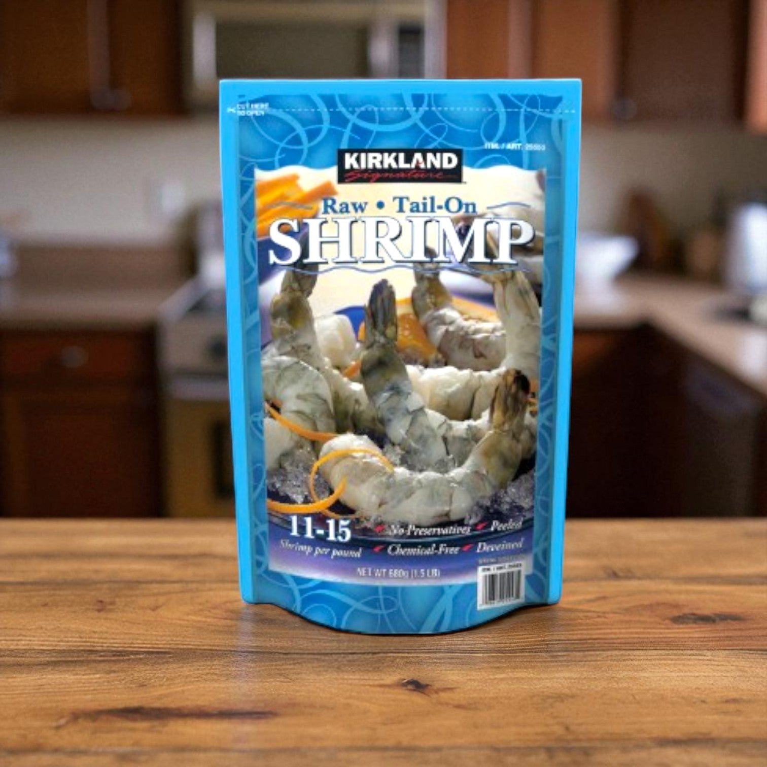 A bag of Kirkland Signature Raw Shrimp-1.5 lbs is displayed on a wooden table in a kitchen, highlighting the Kirkland Signature label and the individually quick frozen shrimp inside.