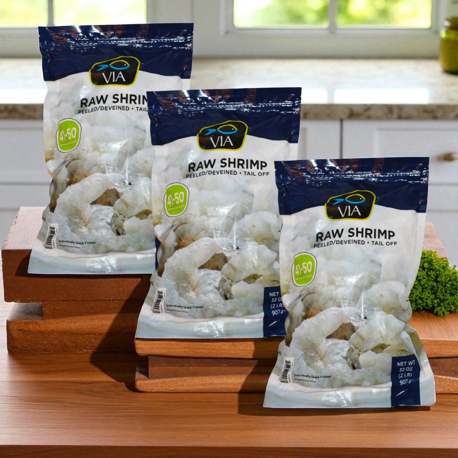 Three bags of Via Farms Farm-Raised Raw Shrimp, Tail-Off, Peeled, Deveined, 41-50 ct, 2 lbs each (3 Count) are displayed on stacked wooden cutting boards in a kitchen setting.