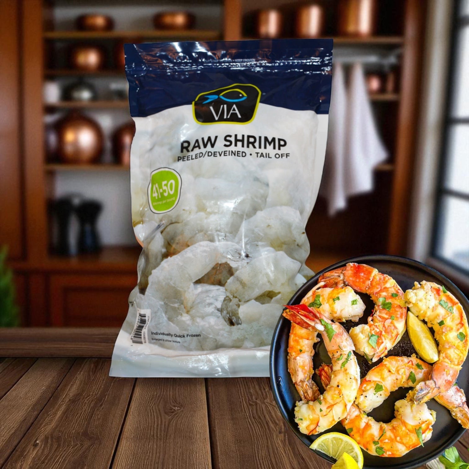 A bag of Via Farms Farm-Raised Raw Shrimp, Tail-Off, Peeled, Deveined (41-50 ct, 2 lbs) rests on a wooden counter beside a bowl of cooked shrimp with herbs and lemon slices. Kitchen shelves appear in the background.