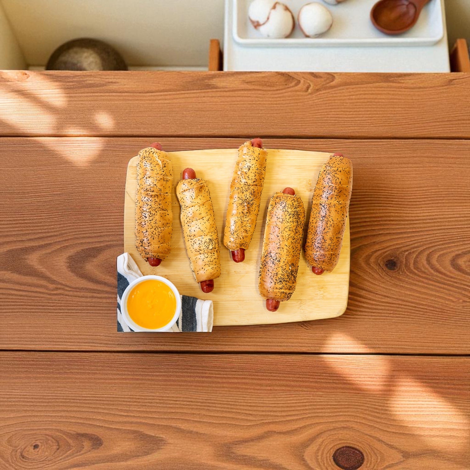 Five Vienna Beef Polish Sausage Bagel Dogs rest on a wooden cutting board, accompanied by a small bowl of yellow dipping sauce on a wooden table.