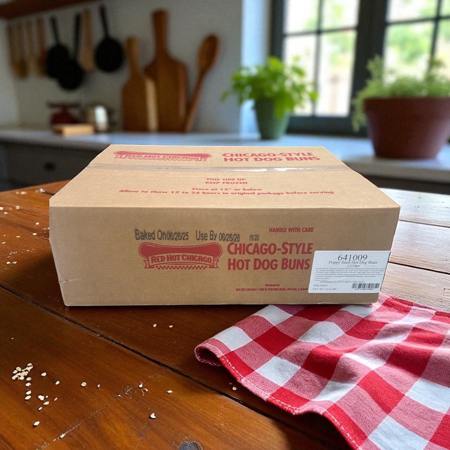 A box of Vienna Beef Poppy Seed Hot Dog Buns 10 Count - 12 Pack sits on a wooden table beside a red and white checkered cloth in a cozy kitchen.