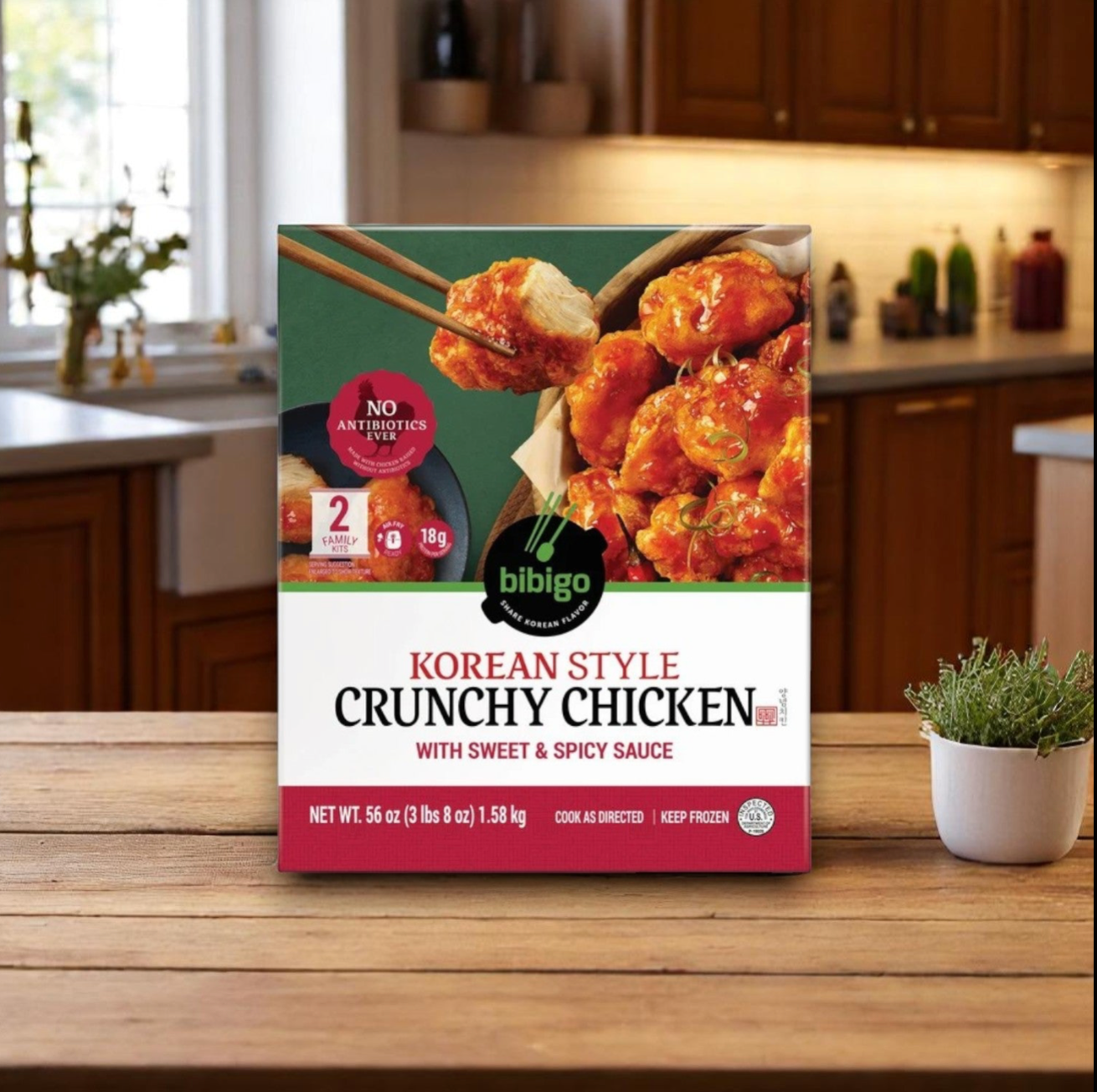 A 56 oz bag of Easy Lunches Bibigo Korean Style Crunchy Chicken with Sweet & Spicy Sauce (3 count) is displayed on a wooden table in a kitchen.