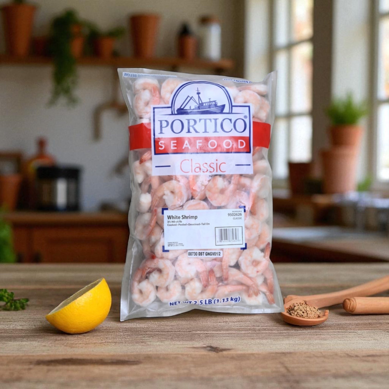 A bag of Sysco Shrimp White Peeled And Deveined Tail-on Cooked 2.5 lb, 4 Count sits on a kitchen counter next to a lemon wedge and a small bowl of brown spice, with blurred kitchen items in the background.