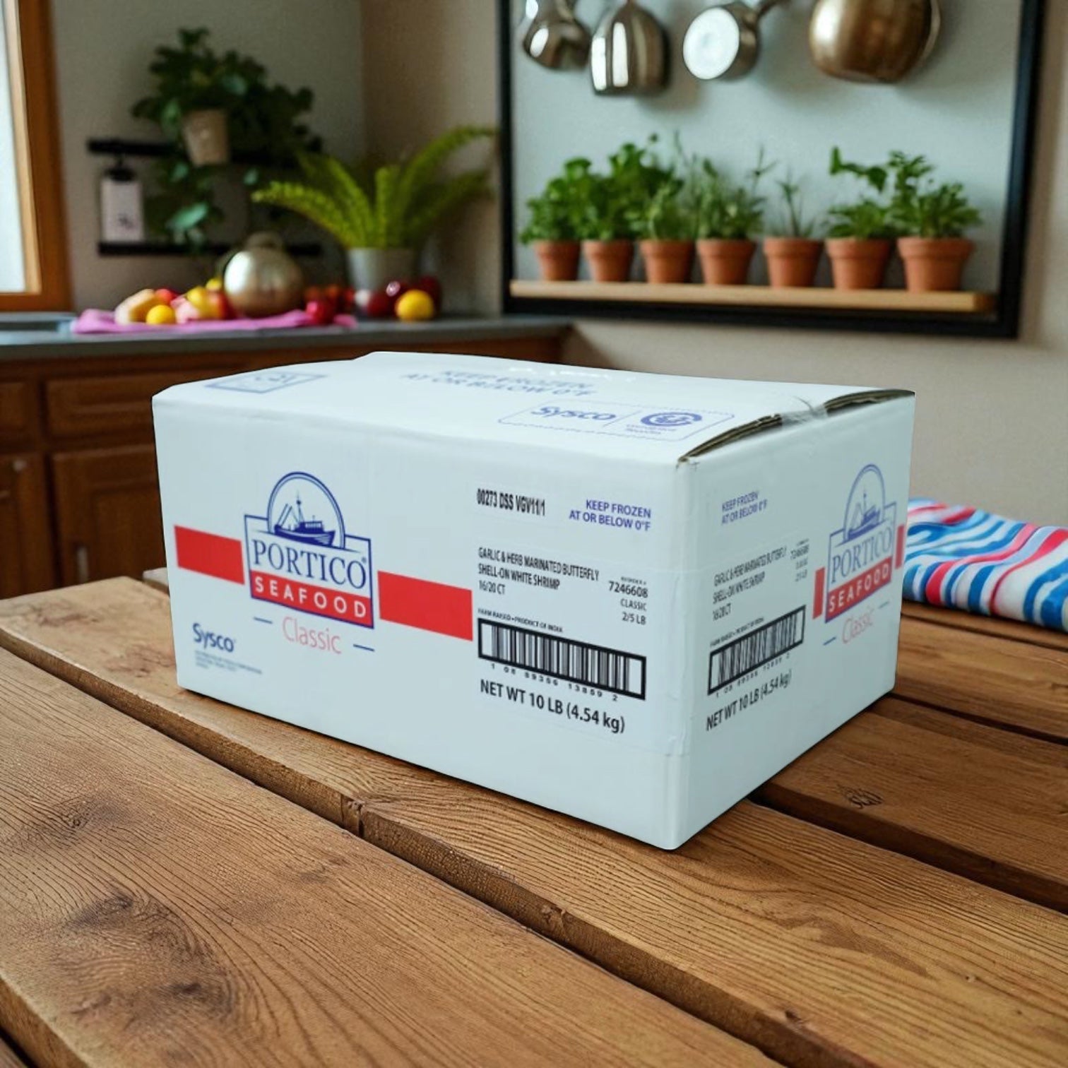 A white 10 lb Sysco box labeled "Shrimp White Peeled And Deveined Tail-on Cooked 2.5 lb Case - 4 Bags" sits on a wooden kitchen table with potted plants and kitchenware in the background, featuring individually quick frozen shrimp.