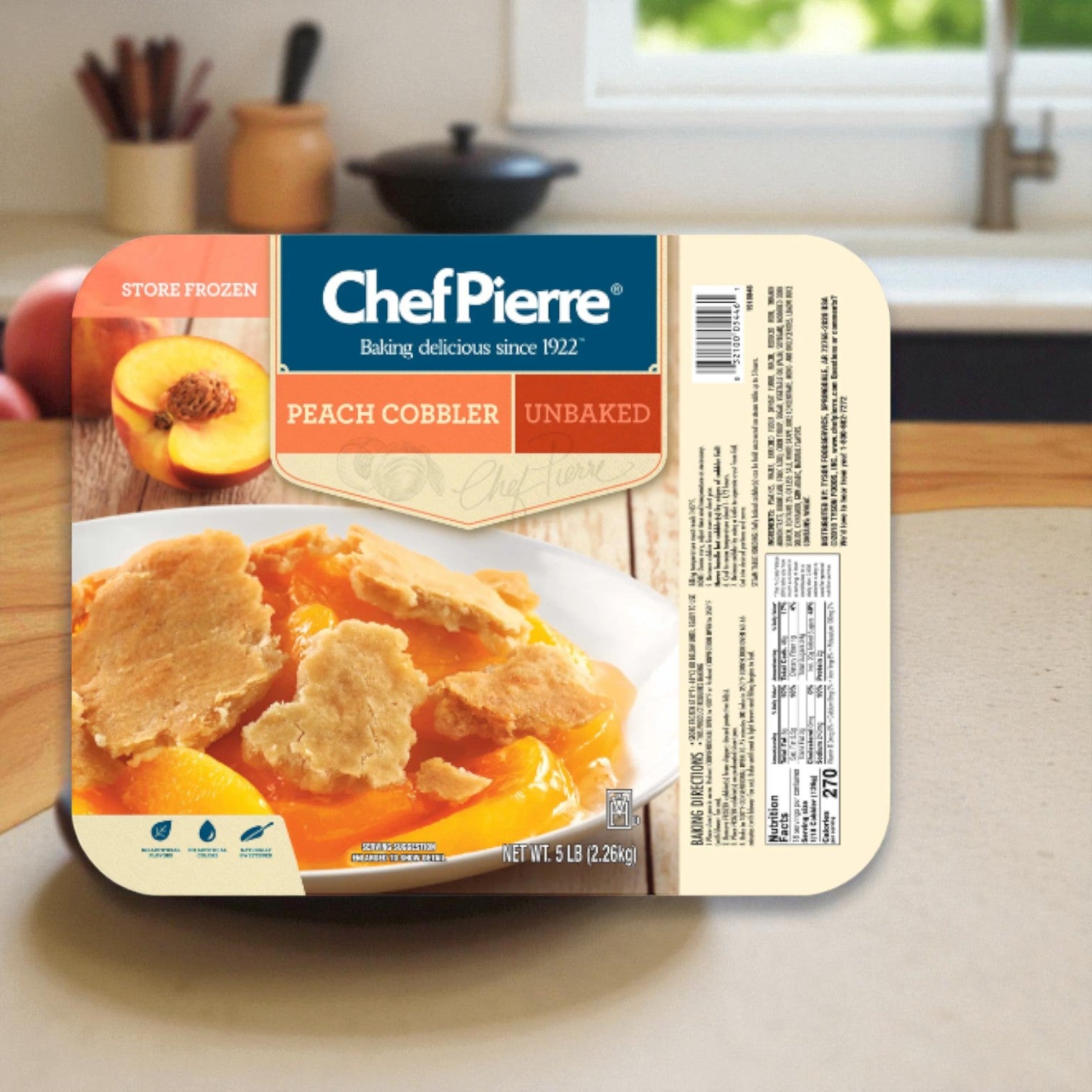 A package of Sara Lee Chef Pierre Peach Cobbler (5 lb, 1 pack) from Chef Pierre rests on a kitchen counter, evoking the feel of homemade cobbler, with a window and sink visible in the background.