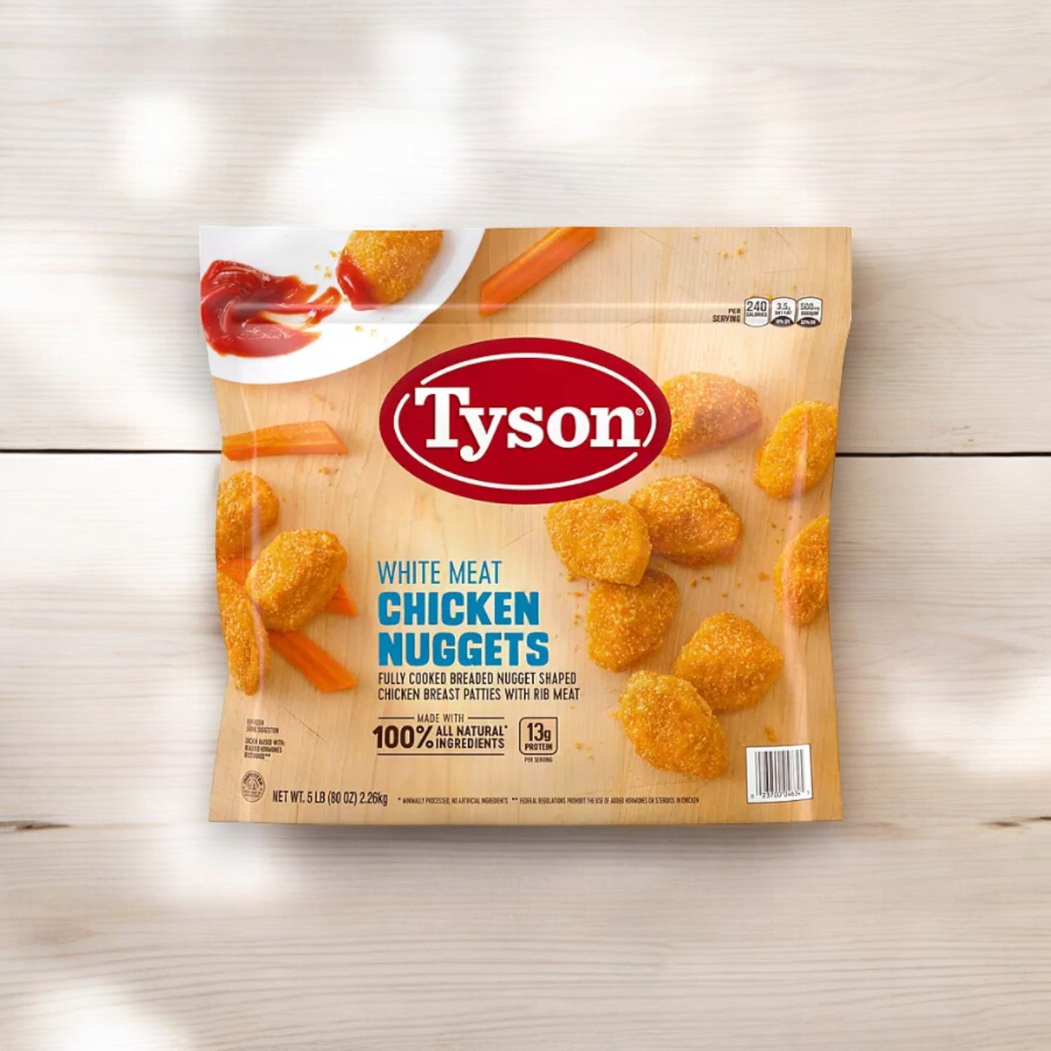 A 5-pound package of Tyson White Meat Chicken Nuggets, Frozen is displayed on a light-colored wooden surface, with a few protein-packed nuggets and carrot sticks dipped in ketchup shown at the top left of the packaging.