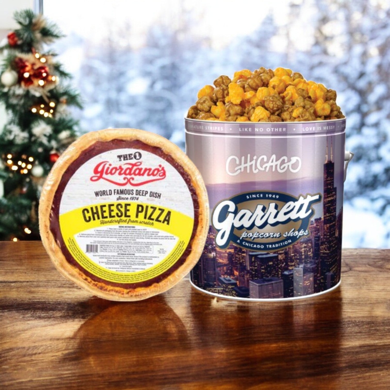 An enticing Chicago's 2 Pack Combo! from Easy Lunches, featuring a deep dish cheese pizza and a large decorative tin of Garrett Popcorn, sits invitingly. Through the snowy window, a beautifully adorned Christmas tree adds a festive touch to this cozy scene.