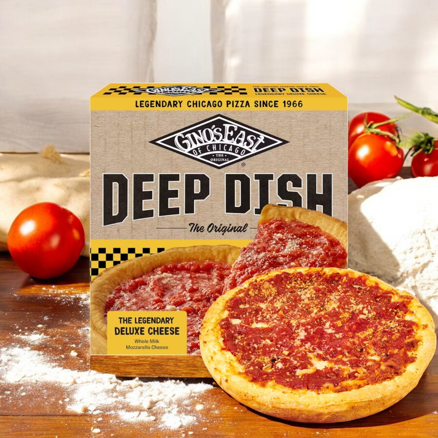 A box of Gino's East Pizza, Deluxe Cheese, Deep Dish-1 Count rests on a wooden surface amid fresh tomatoes and dough, offering an authentic deep-dish experience.
