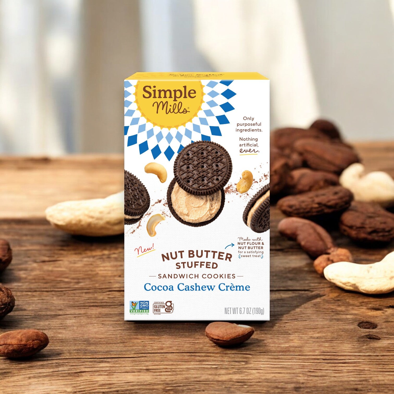 A box of Simple Mills Nut Butter Stuffed Sandwich Cookies, Cocoa Cashew Creme (6.7 oz), is placed on a wooden surface, surrounded by cashews and cocoa beans. The Gluten-Free, Non-GMO packaging emphasizes pure ingredients that are suitable for vegans.