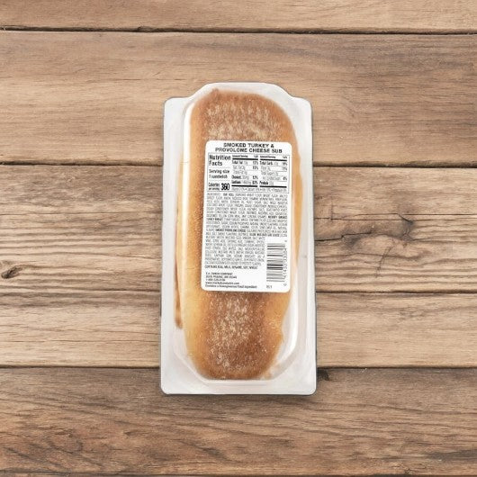 A packaged sub sandwich labeled as "Smoked White Turkey & Provolone Cheese Sub" by E.A. Sween, rests on a wooden surface. The label on the packaging contains nutritional information and ingredients.