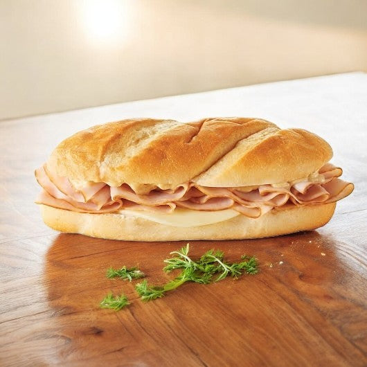 An E.A. Sween Smoked White Turkey & Provolone Cheese Sub, featuring delectable smoked white turkey and creamy provolone cheese inside a crusty roll, placed on a wooden surface with a small bunch of green herbs in the foreground.