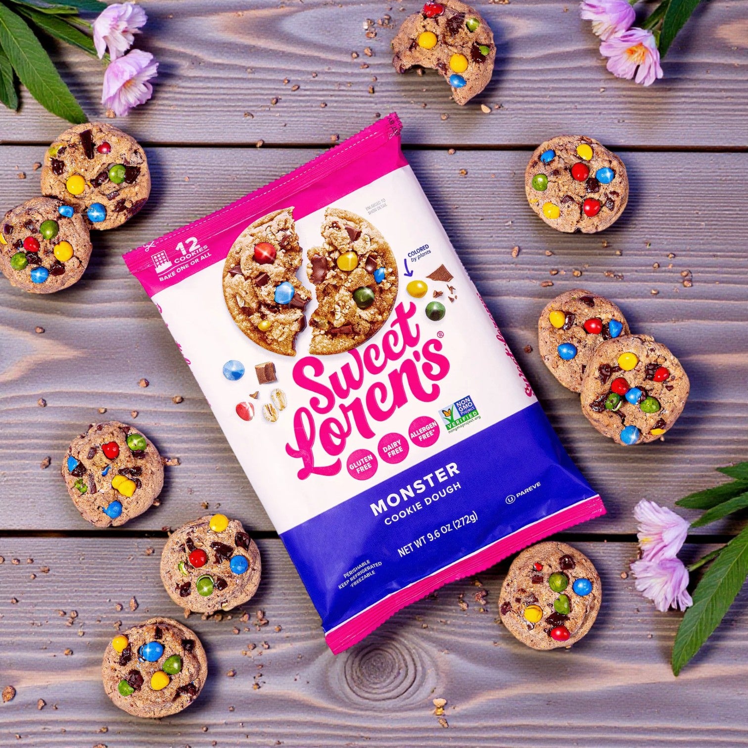Sweet Loren’s Cookie Dough Combo—Monster Cookie Dough (9.6 oz) and Chocolate Chunk Cookie Dough (12 oz, gluten-free & vegan)—is shown among baked cookies with colorful candy pieces on a wooden surface with scattered flowers and leaves.