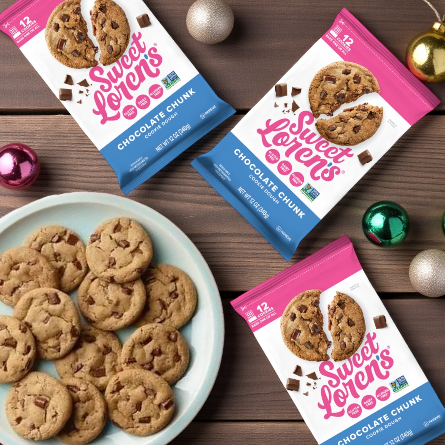 Three packs of Sweet Loren’s Chocolate Chunk Cookie Dough – Gluten-Free & Vegan, 12 oz each, from Sweet Loren's are displayed on a wooden table with vegan cookie treats and holiday ornaments.