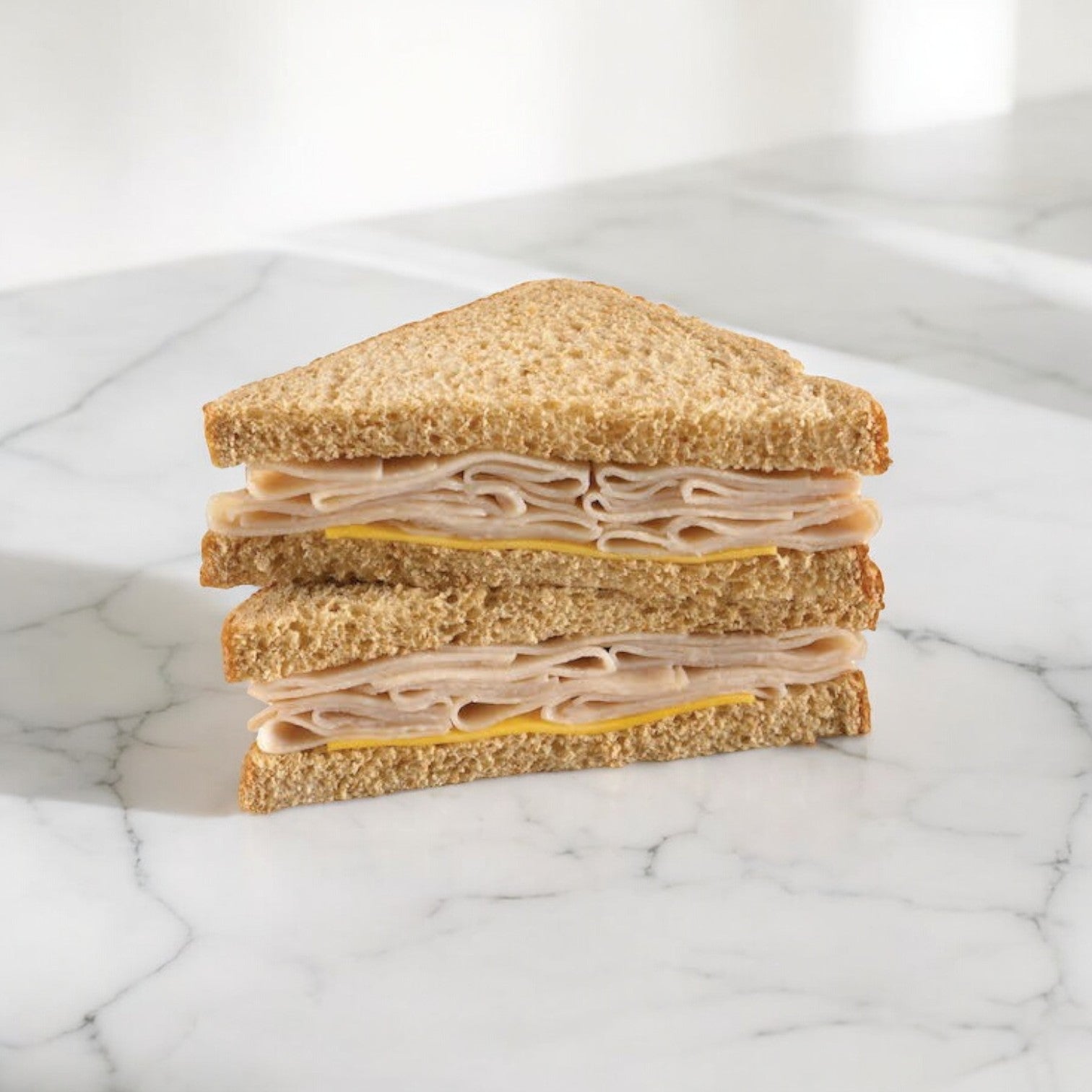 An Oven Roasted Turkey & Cheese Sandwich Wedge from E.A. Sween, made with whole wheat bread and featuring layers of sliced deli meat and cheese, cut into triangles, placed on a marble surface.