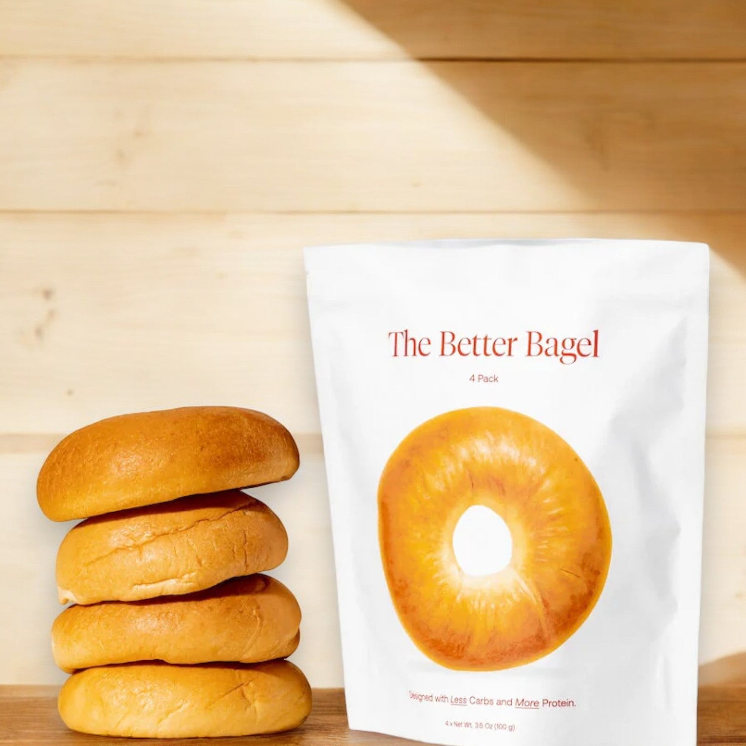 A stack of three bagels with a chewy interior sits next to a white package labeled "BetterBrand - The Better Bagel - The Classic," displaying an image of a Classic Bagel on the front.