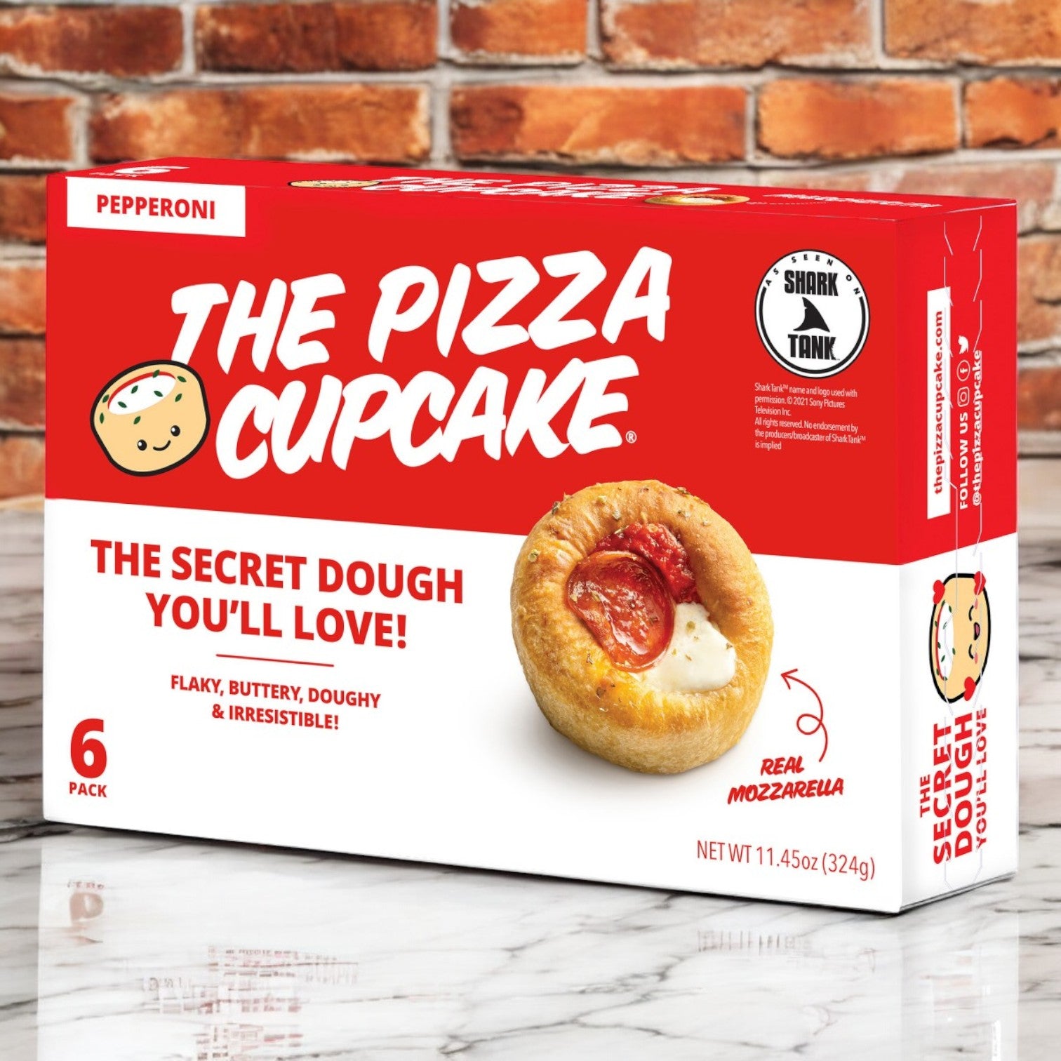 A box of "The Pizza Cupcake" by The Pizza Cupcake brand offers six pepperoni-flavored pastries, ideal for on-the-go snacking. Featuring the label "The Secret Dough You'll Love!" and made with "Real Mozzarella," it is beautifully set against a brick background.