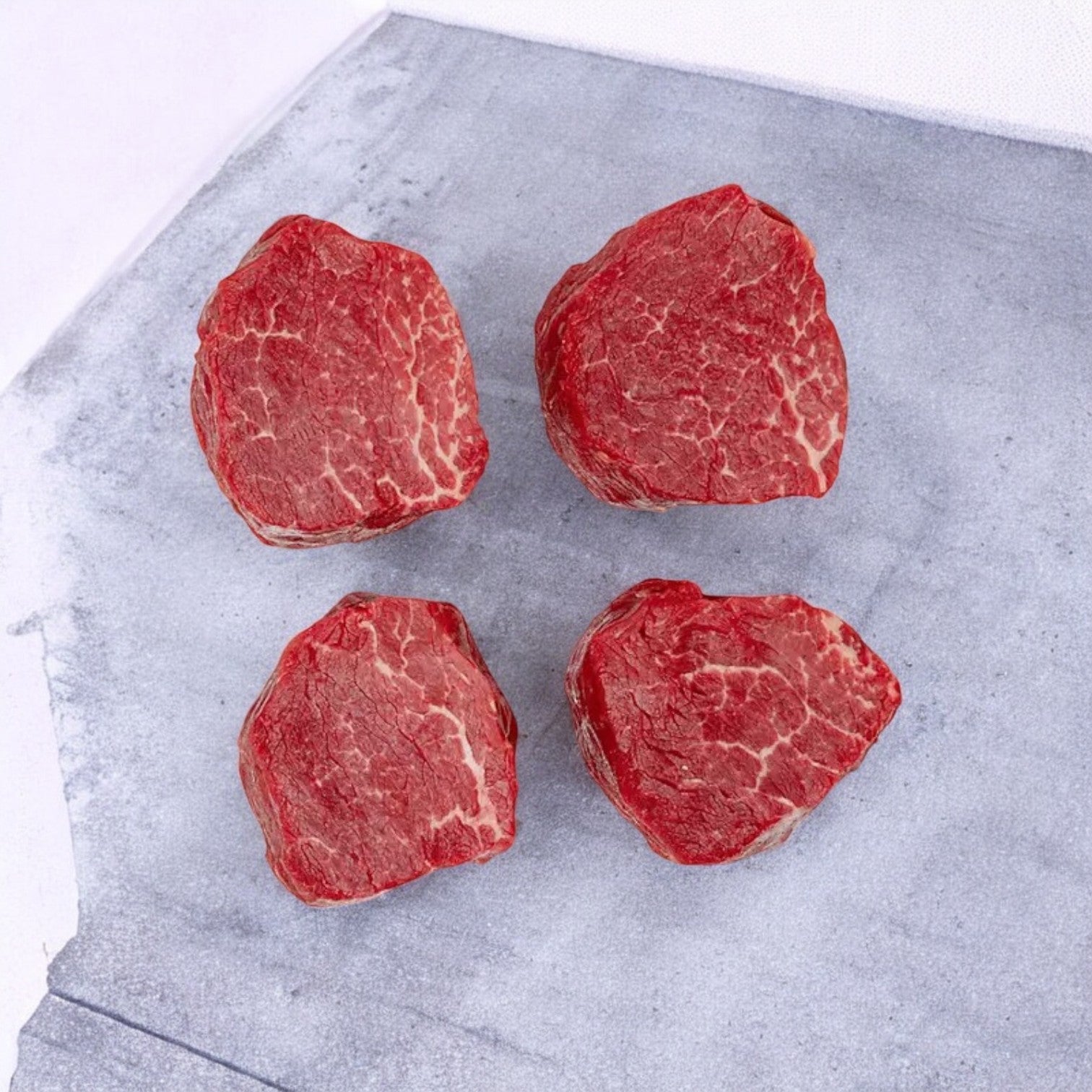 Three packs of Thomas Farms' Tenderloin Beef Steaks, a premium choice known for gourmet dining experiences, featuring 12 grass-fed steaks, are placed on a gray stone surface with free shipping included.