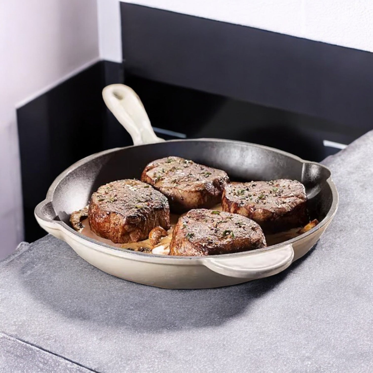 A cream-colored skillet holds four Thomas Farms Tenderloin Beef Steaks, sizzling on a stone surface and offering a perfect gourmet dining experience.