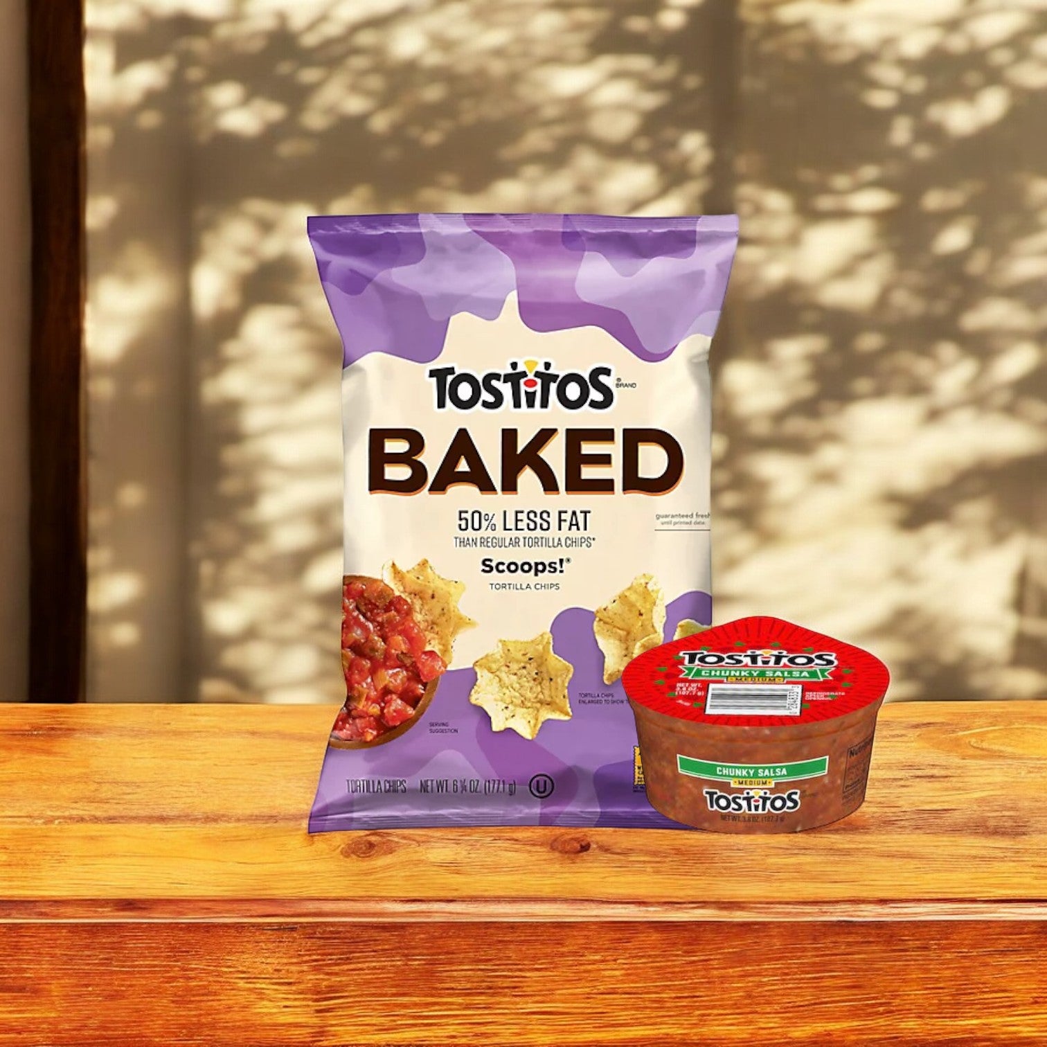 A Tostitos Baked Scoop with Tostitos Chunky Salsa sits on a wooden surface against a blurred background.