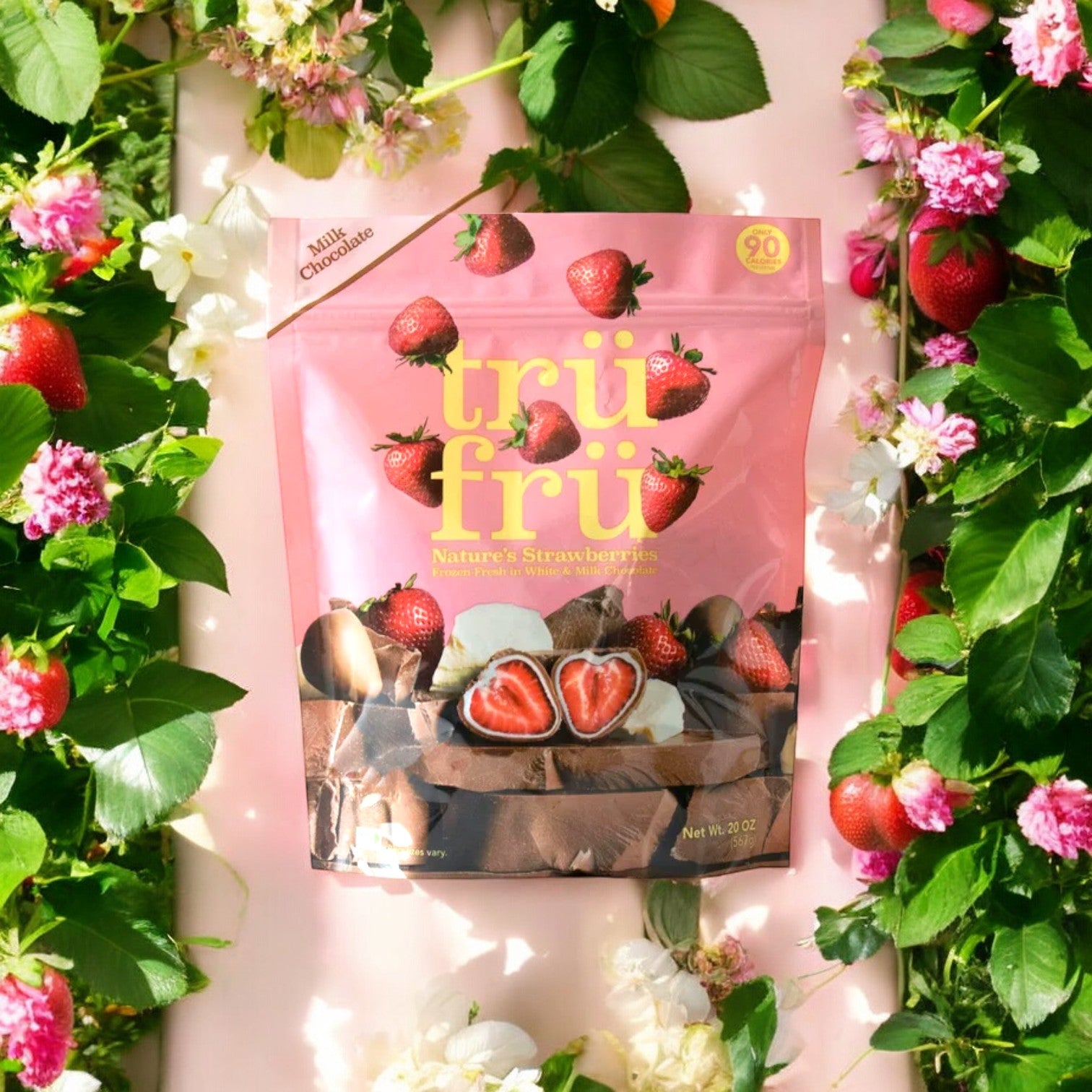 A 20 oz. bag of Tru Fru Milk Chocolate Strawberries, 1 Count, surrounded by flowers. The pink packaging features images of juicy, freeze-dried strawberries and chocolate, with the product labeled as Tru Fru Milk Chocolate.