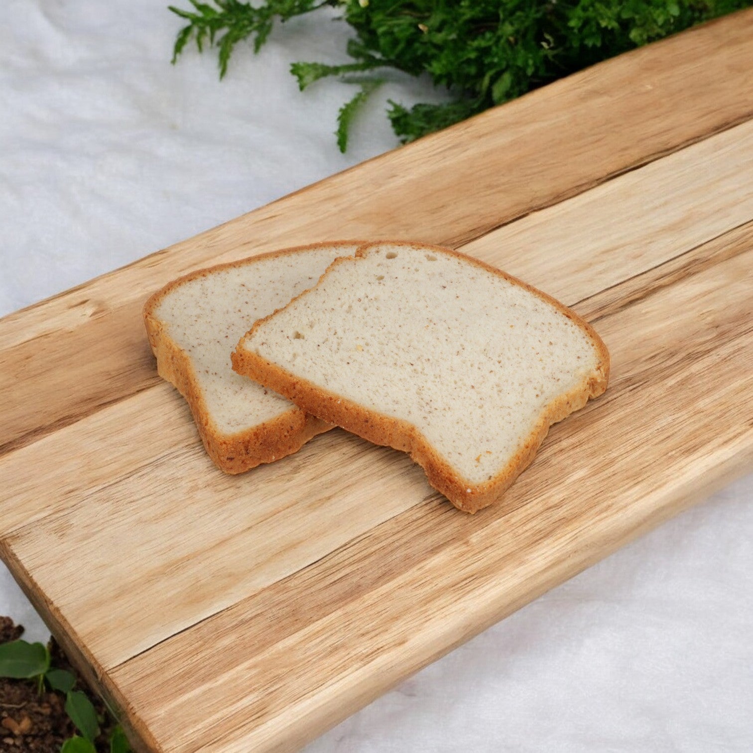 Two slices of Udi's multigrain gluten-free bread loaf rest on a wooden cutting board, with greenery in the background.