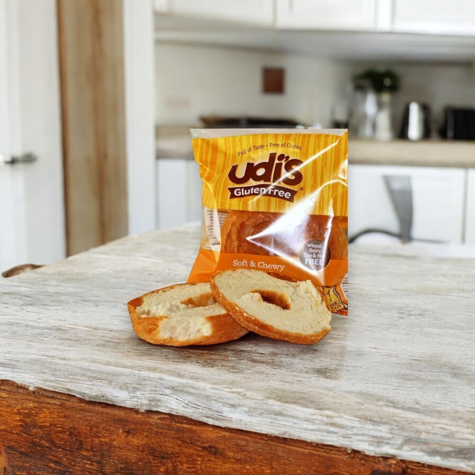 A sliced Udi's Plain Bagel, 3.5 oz. - 1 Count, renowned for its classic flavor and texture, is placed in front of its packaging on a wooden surface in a kitchen setting.