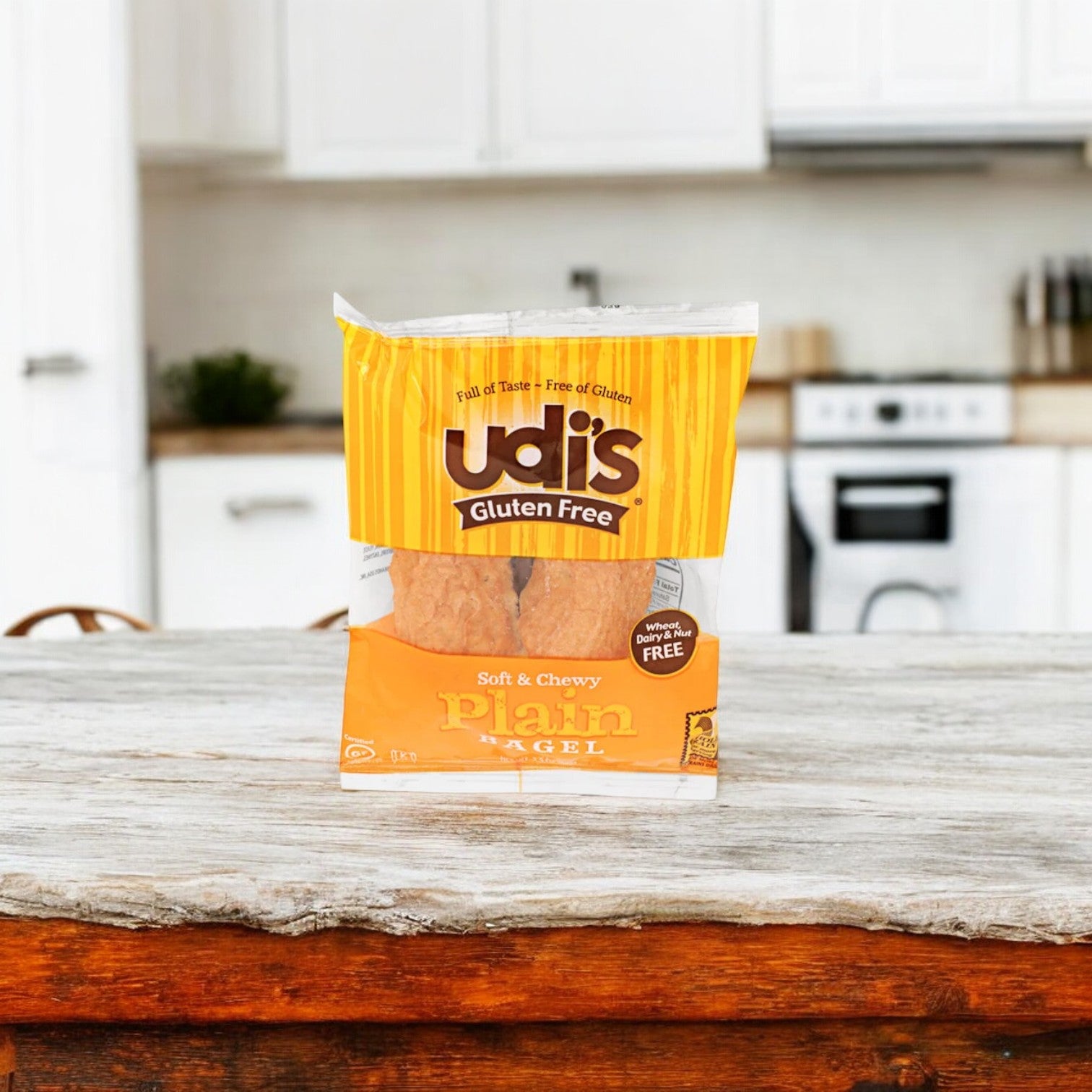 A package of Udi's Plain Bagel, 3.5 oz. - 1 Count, sits on a wooden counter in a kitchen with white cabinets and countertops, promising classic flavor and texture.