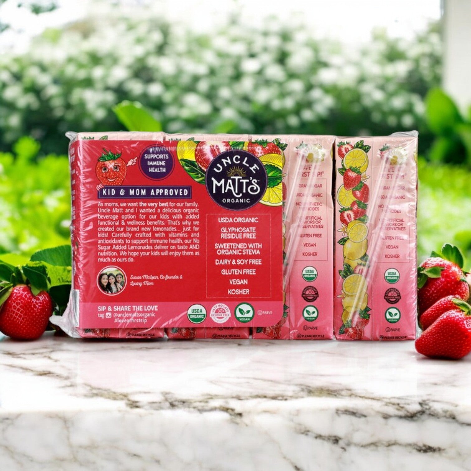 Uncle Matt's Organic offers an 8-pack of No Sugar Added Strawberry Lemonade Juice Boxes (6.75 fl oz each) that are USDA organic, gluten-free, vegan, and enhanced for immune support, featuring a backdrop of fresh strawberries and greenery.