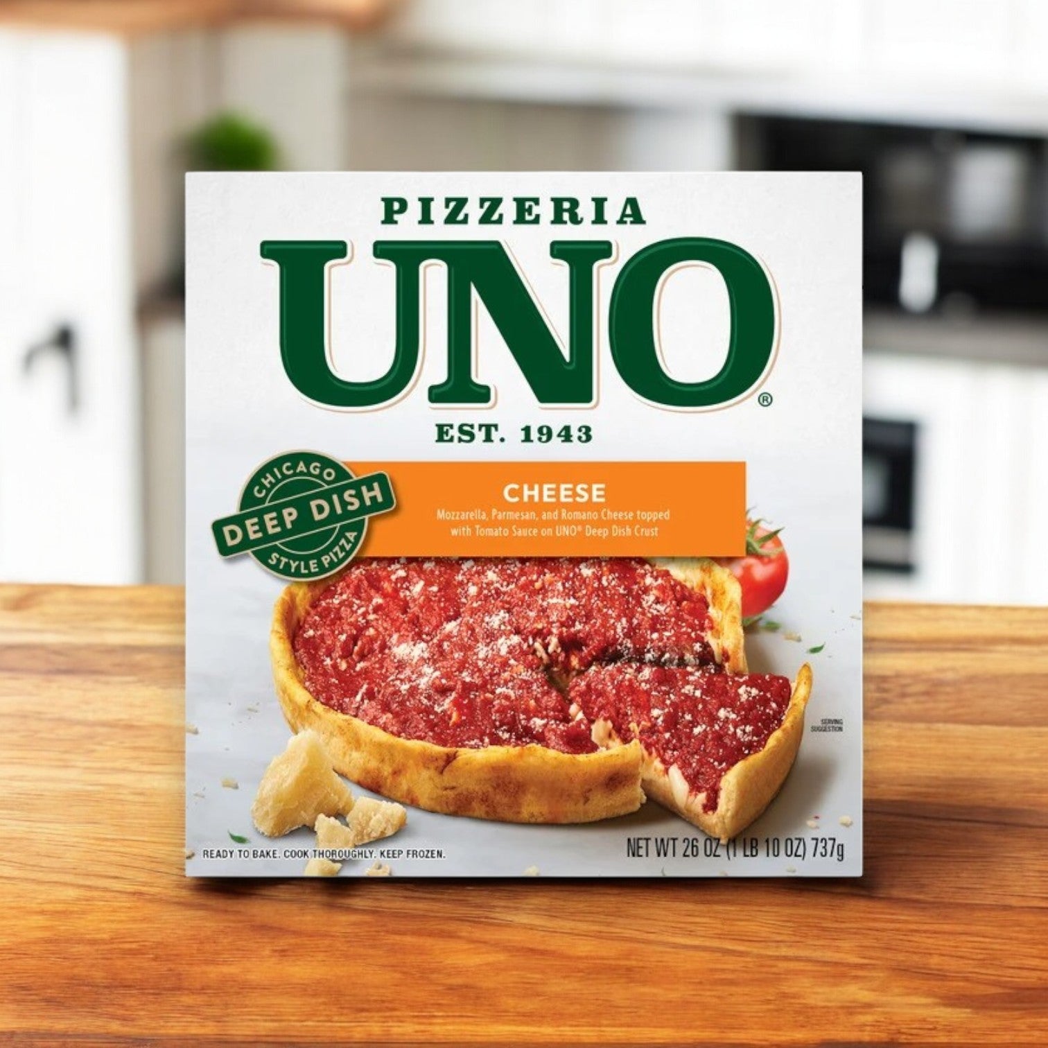 A box of Pizzeria Uno Deep Dish Trio—featuring Classic Sausage, Cheese & Prima Pepperoni pizzas—rests on a wooden table in a cozy kitchen setting.