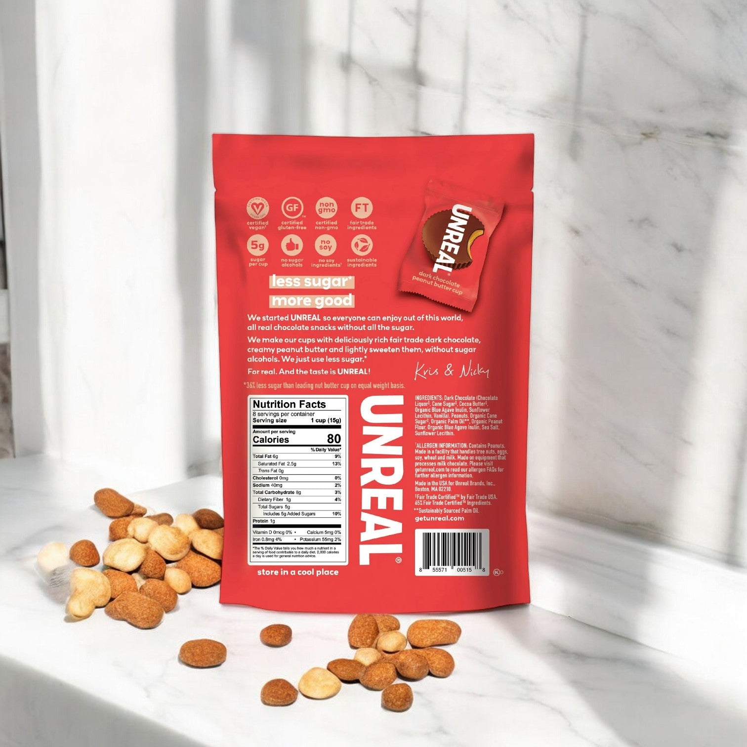 An Unreal Dark Chocolate Peanut Butter Cups bag, weighing 4.2 oz and bright red in color, is displayed on a marble surface with scattered peanut butter cups beside it. The packaging highlights “less sugar” and nutritional facts on the back and also proudly marks that it is gluten free.