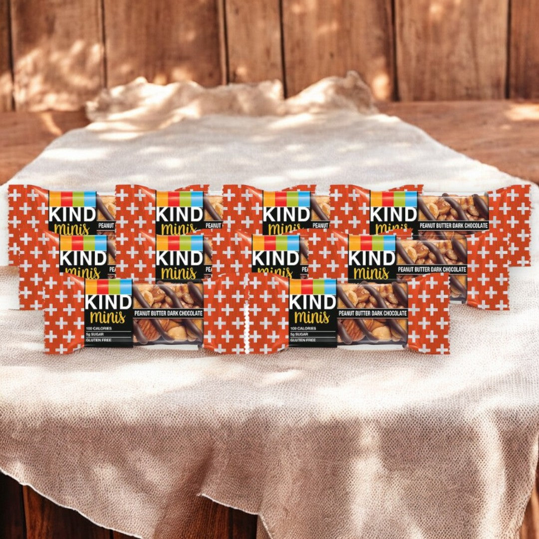 Boxes of Kind Minis Peanut Butter Dark Chocolate - 10 Count from Kind are displayed on a white cloth on a wooden table, making for a perfect healthy snack.