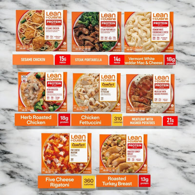 A display of Lean Cuisine frozen meal boxes arranged in three rows on a marble surface, featuring a variety pack of nutritious meals including Sesame Chicken, Steak Portabella, Vermont White Mac & Cheese, Herb Roasted Chicken, Chicken Fettuccini, Meatloaf, Five Cheese Rigatoni, and Roasted Turkey Breast.