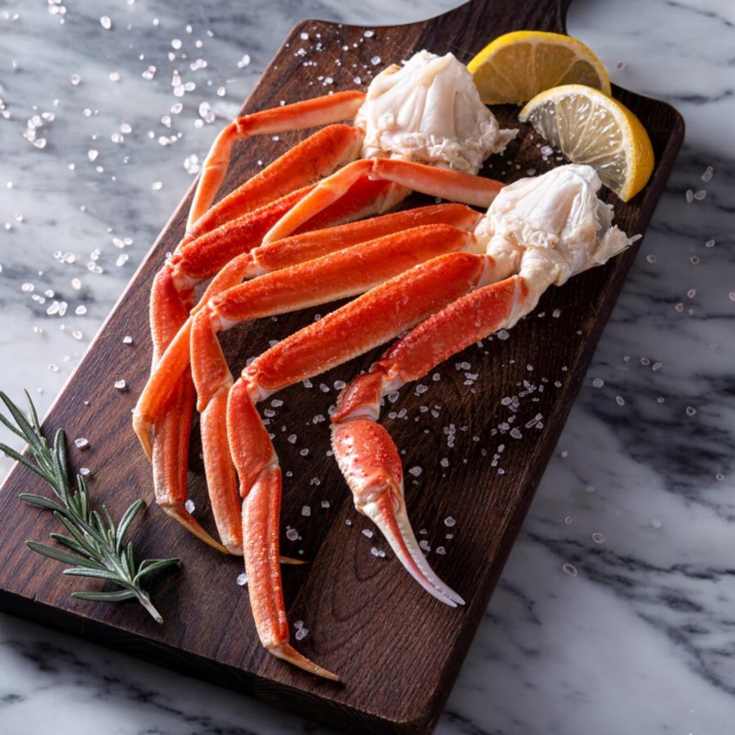 Robisea Wild Caught Snow Crab Clusters by Easy Lunches, paired with lemon wedges and rosemary, are displayed elegantly on a wooden board, sprinkled with sea salt, atop a marble surface.