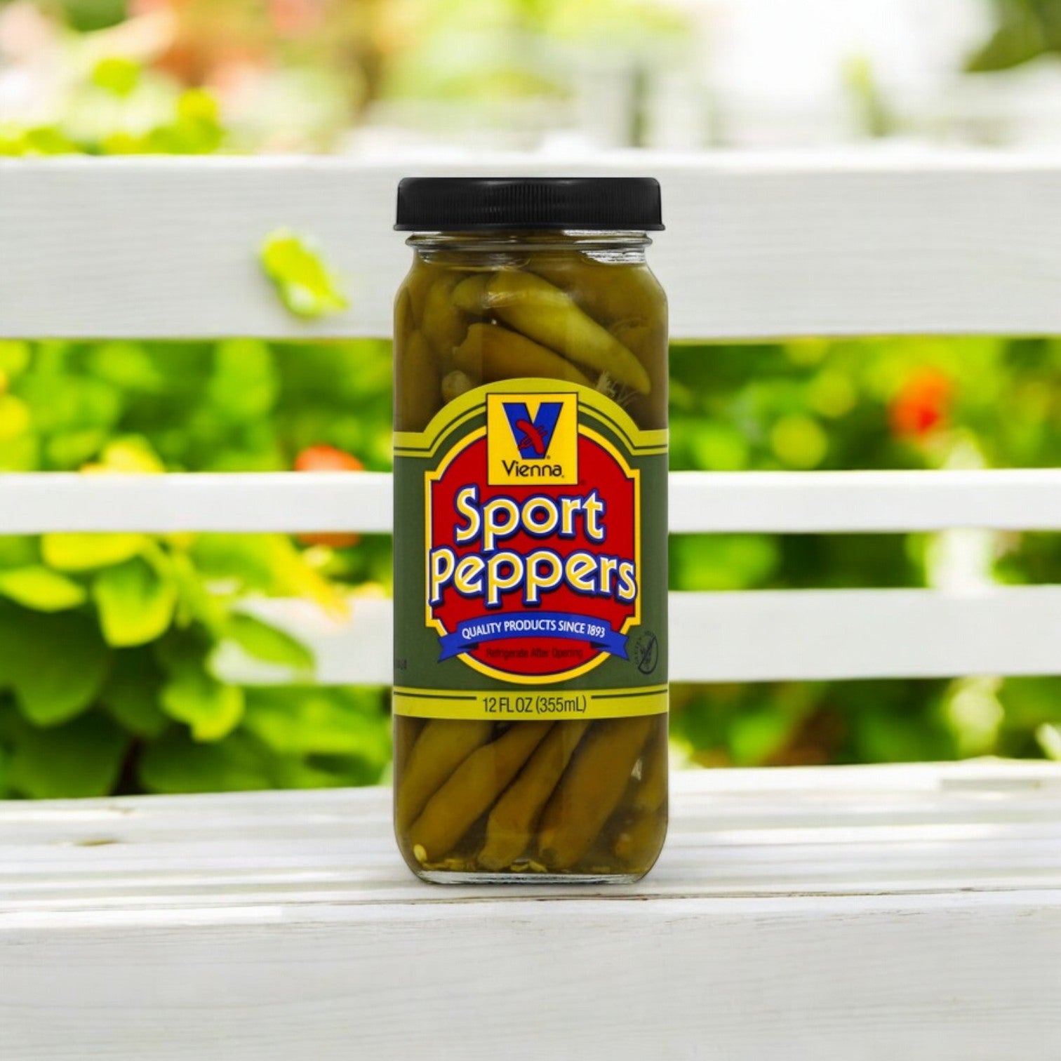 A 12 oz. jar of Vienna Beef Sport Peppers, ideal for Chicago-style hot dogs, sits on a white wooden surface with blurred greenery in the background. The label features blue and yellow colors with red lettering.