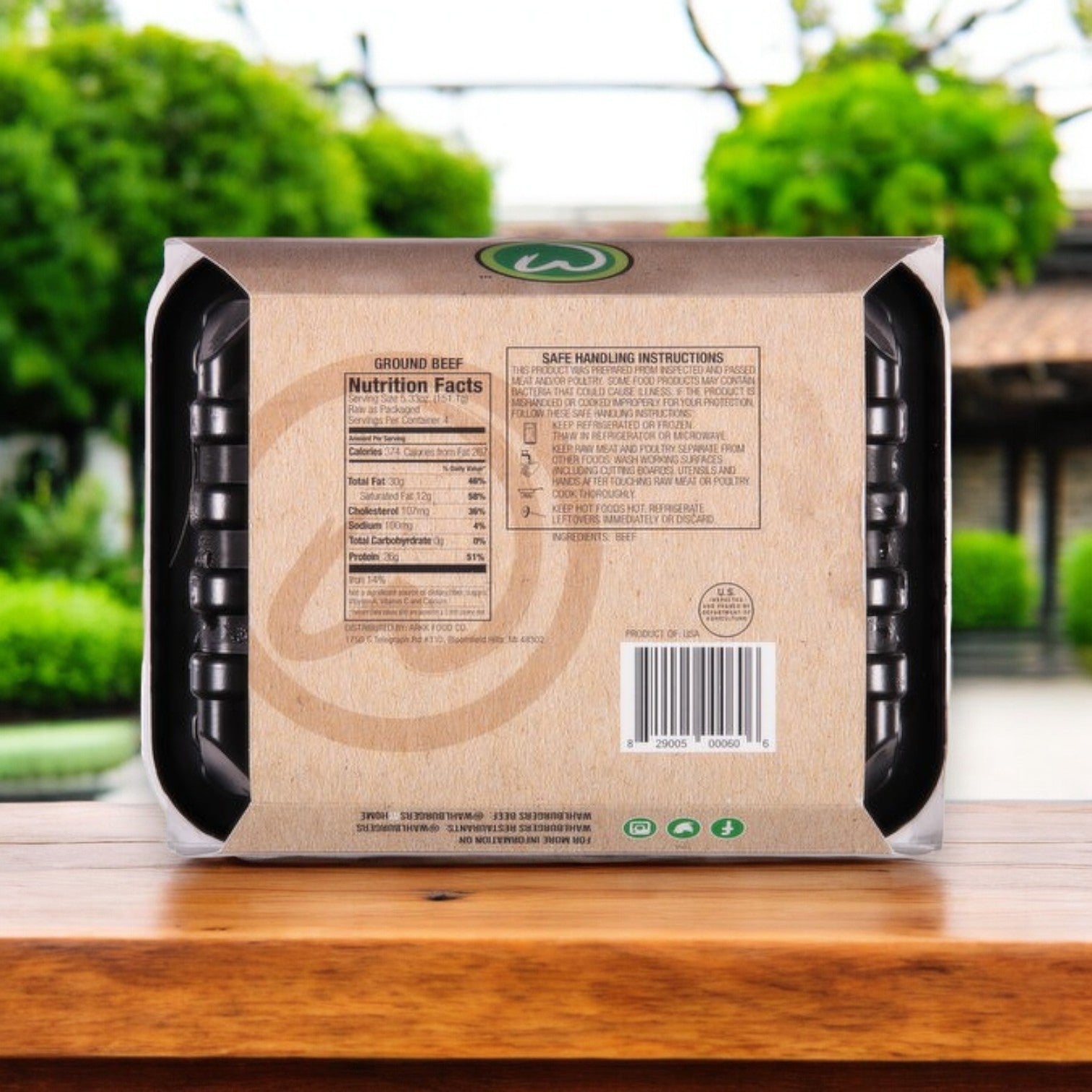 A pack of Wahlburgers Famous Gourmet Blend Fresh Angus Burgers, 21.32 oz - 3 Count, sits on a wooden table with nutrition facts and safe handling instructions visible. Picture these gourmet burgers enhancing your grilling experience against a blurred outdoor greenery backdrop.