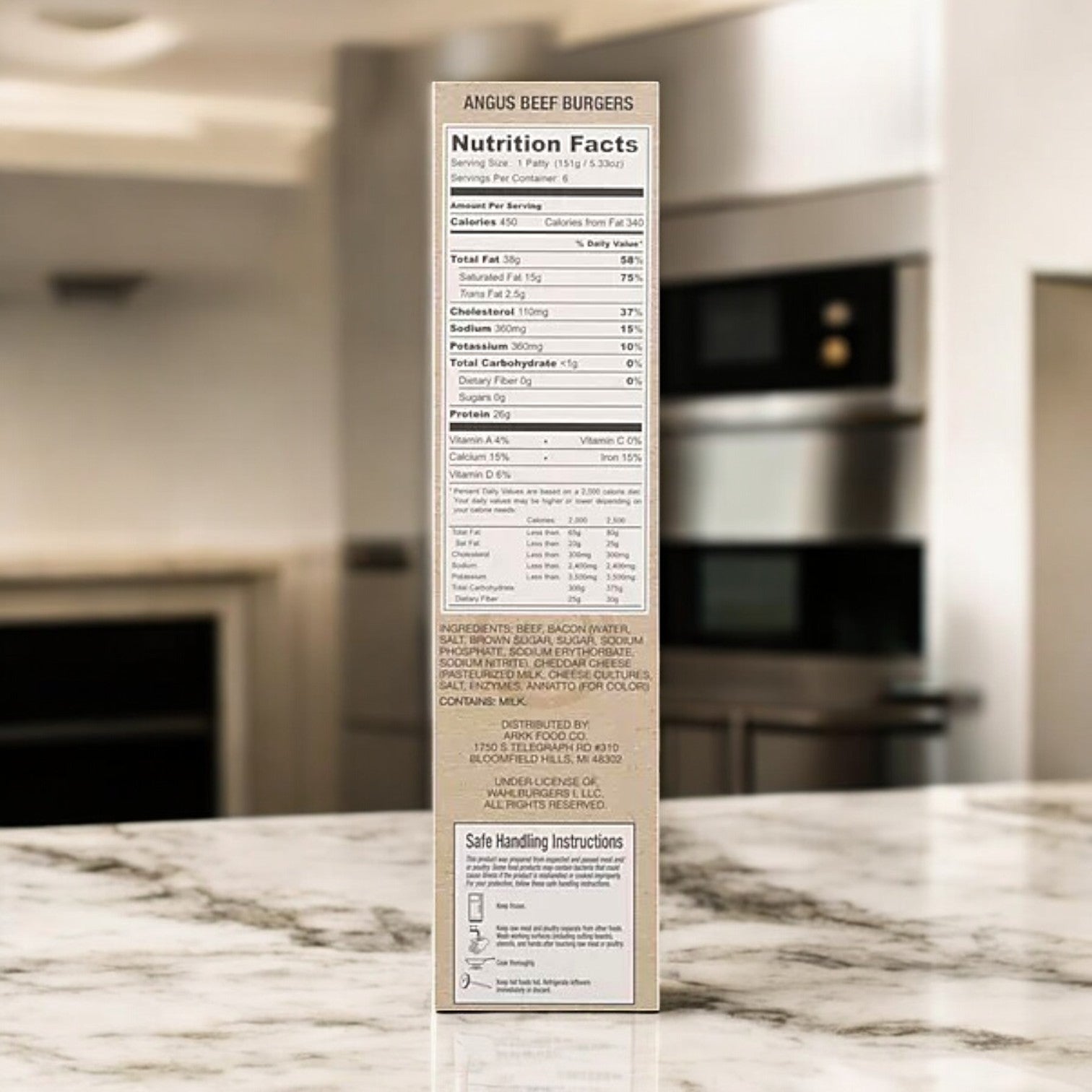 A box of Wahlburgers Frozen Beef Patties, Bacon & Cheddar, 32 oz, sits on a marble counter with nutrition facts and safe handling instructions visible. Kitchen appliances in the background hint at the savory Angus beef flavor from Wahlburgers.